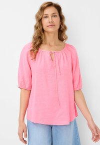 Blusa rosa realizzata in tessuto leggero con maniche a sbuffo 3/4, scollatura a chiave con dettaglio di legatura e un taglio leggermente cropped.