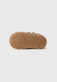 Brun gummisåle med teksturert grep, med preget logo og spor for bedre veigrep. Mykt beige overmateriale synlig på sidene.