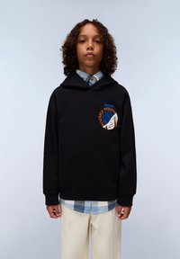 Zwarte hoodie met een voorzak, voorzien van een kleurrafische "Onderzoeksprogramma" graphic. Gedragen over een blauw geruit shirt en lichte broek.