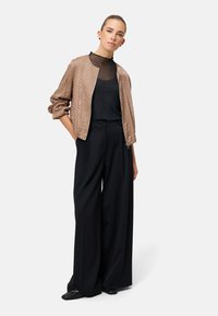 Beige satin bomberjakke med en tekstureret finish; kombineret med en gennemsigtig sort top og sorte bukser med vide ben; minimalistisk design, elegant silhuet.