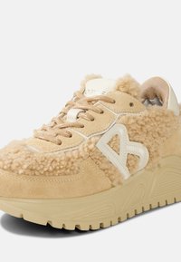 Beige semišové tenisky s huňatou texturou, s bílým logem, smetanovými tkaničkami a masivní gumovou podrážkou pro lepší přilnavost a podporu.