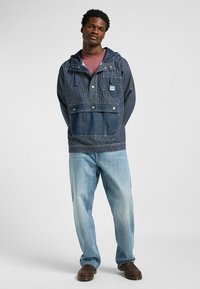 Blauer Denim-Pulloverjacke mit Streifenmuster, Fronttasche und Kapuze. Kombiniert mit hellblauen Jeans und dunkelbraunen Schuhen.