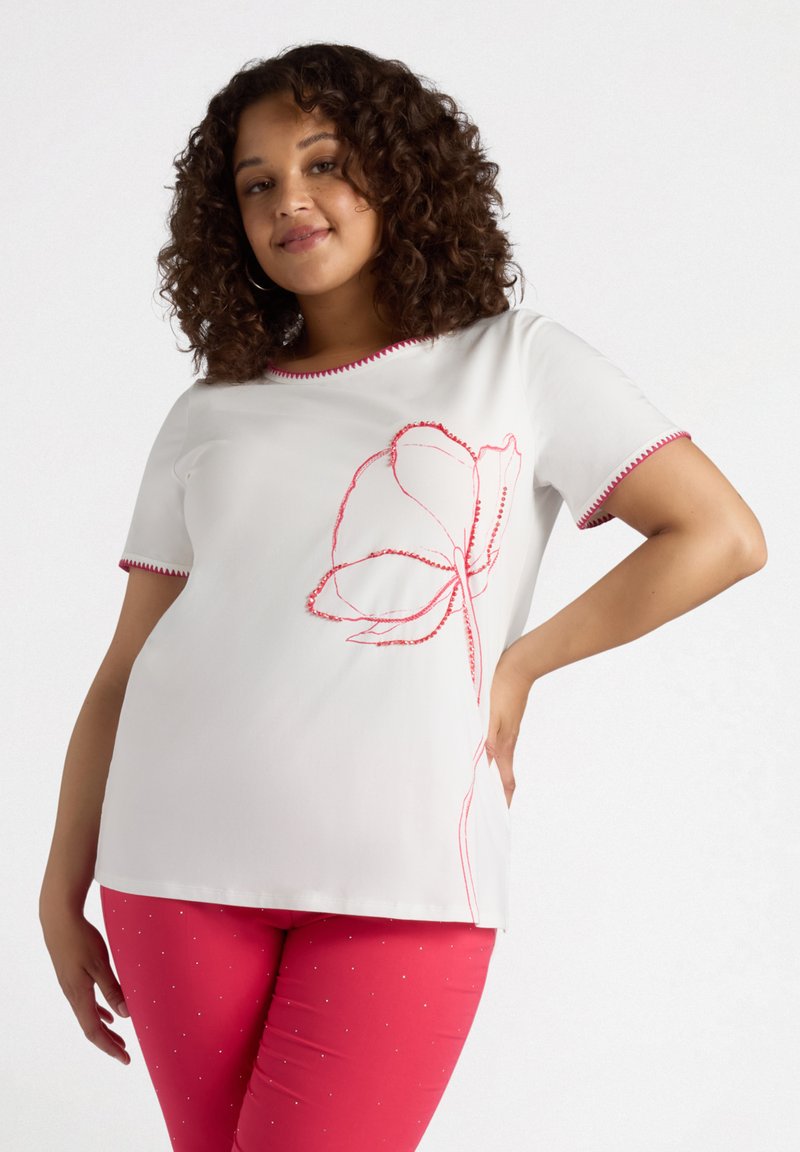 Top corto de manga corta blanco con bordado floral rojo y cuello de contraste. Combinado con pantalones rosas que presentan pequeños adornos.