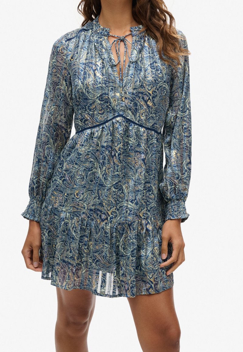 Robe bleue à motifs avec un design cachemire, manches longues, poignets froncés, col à nouer et ourlet évasé à volants.