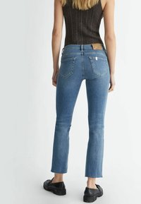 Blå denimjeans med utbuktade benslut, mörk sömnad och två bakfickor. Bärs med en strukturerad, mörk tanktopp och svarta skor.