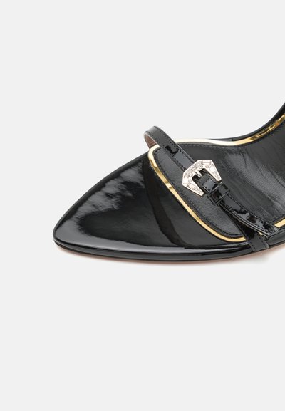 Zapato de charol negro con punta afilada, un estrecho tirante para el tobillo y detalle de hebilla plateada. El interior presenta un sutil patrón texturizado.