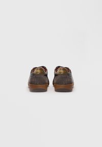 O pereche de adidași din suede și piele maro închis cu tălpi din cauciuc, văzuți din spate, arătând numele de brand "Blauer USA" pe tab-urile călcâiului.