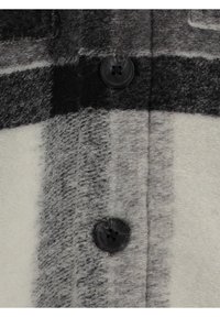 Grau- und weiß kariertes Gewebe mit einer unscharfen Textur, verziert mit schwarzen Knöpfen und auffälligen horizontalen und vertikalen Streifen.