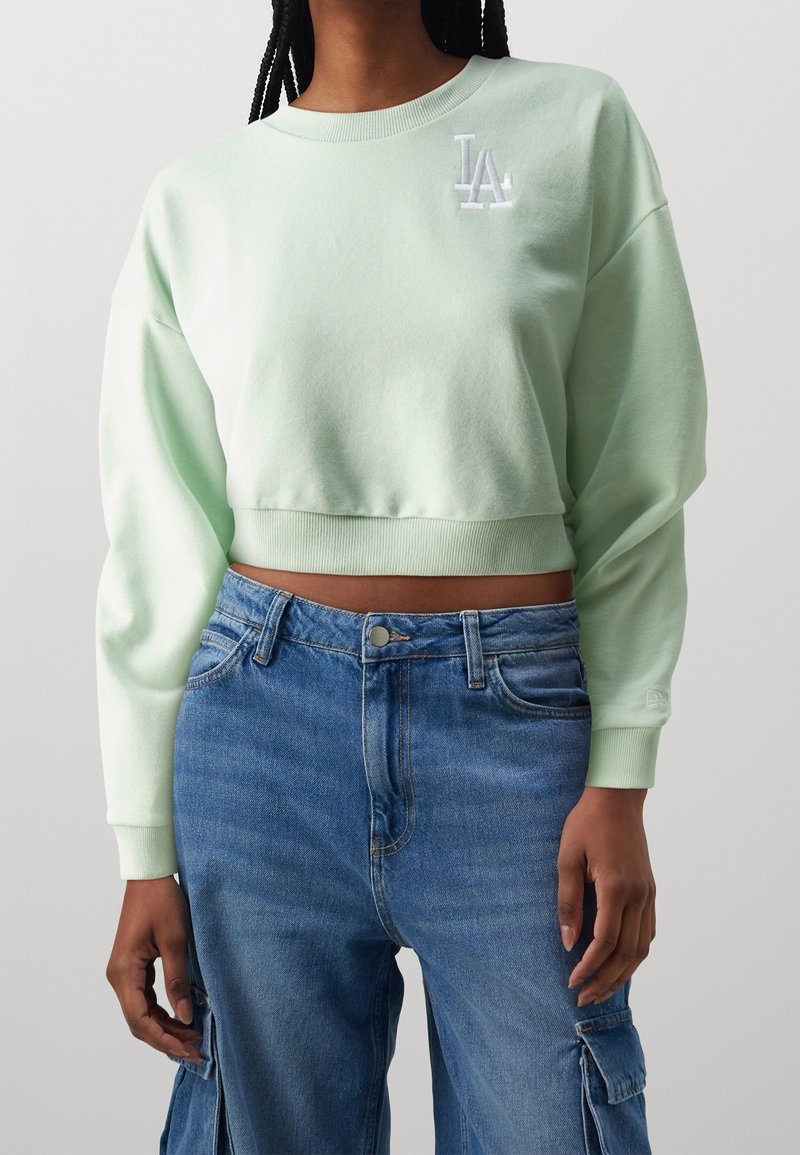 Felpa corta verde menta con scollatura tonda, orlo a coste e logo ricamato "LA". Abbinata a pantaloni cargo in denim azzurro strappato.