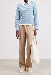 Maglione a righe azzurre chiare con orlo a coste, camicia bianca sotto, pantaloni beige e borsa a tracolla color crema; sneakers con accenti beige.