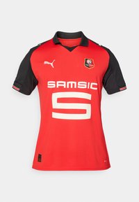Maglia sportiva rossa con maniche nere, caratterizzata da un grande numero 5 bianco, logo "SAMSIC" e emblema del Stade Rennais.