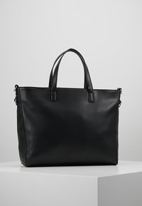 Svart läder tote-väska med en texturerad yta, strukturerad form, två handtag upptill och detaljer i guldton.