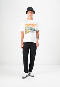 White graphic t-shirt with colorful "SONIC PACE" print, black lightweight pants, and a black bucket hat; white and gray sneakers.