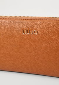 Portafoglio in pelle marrone con superficie texturizzata e logo "LIUJO" in tonalità oro. Presenta una chiusura con cerniera lungo il bordo superiore.