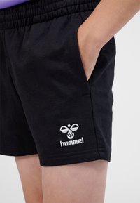 Pantaloncini neri in cotone con vita elastica, tasche laterali e logo "hummel" ricamato in bianco vicino all'orlo. Design semplice e tessuto morbido.