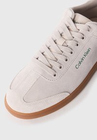 Sneaker en daim gris clair avec une semelle en caoutchouc gomme. Équipé de lacets ronds et d'un accent de logo vert. Bout arrondi et design épuré.