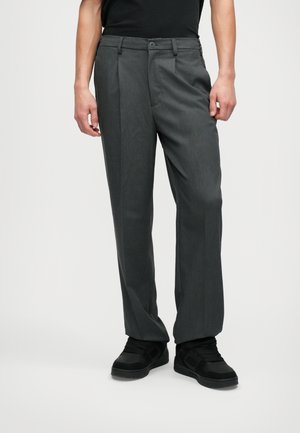 Sive hlače s ravnim krojem, narejene iz strukturirane tkanine. Imajo gumb za zapiranje in sprednje zgube. Ujemajo se z črnimi supergami.