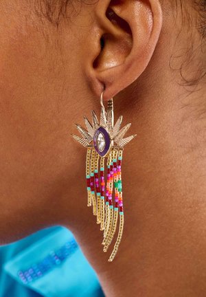 Boucles d'oreilles dorées au design en éclat de soleil, ornées d'accents en pierre violette et transparente, embellies de franges colorées en perles dans divers motifs.