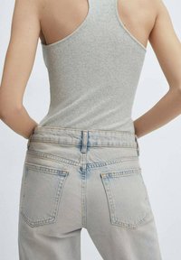 Un top de damă de culoare gri deschis, cu dungi, purtat cu blugi evazați de culoare albastră, cu talie înaltă, având două buzunare la spate și detalii de cusătură subtile.