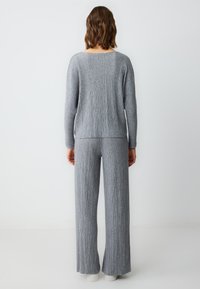 Grijze geribde gebreide trui en bijpassende broek, met lange mouwen en wijde pijpen. Zachte textuur met subtiele verticale strepen.
