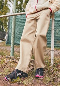 Beige, loose-fitting pants made of cotton blend, featuring a small red Nike logo. Paired with black and pink Nike sneakers.