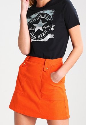 Musta lyhythihainen t-paita, jossa on graafinen tähti-kuvio. Oranssi denimmekko, jossa on kaksi etutaskua ja kullanväriset kiinnikkeet.