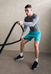 Hallhalli, halli keskkonnas on seljas hall pika varrukaga sportlik särk, türkiissinised lühikesed püksid ja mustad treeningkingad valgete aktsentidega, kasutades musti võitlusköisi.