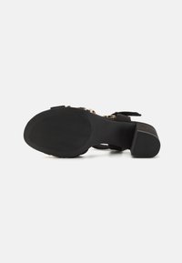 Sandale à talon en daim noir avec une semelle texturée, présentant un design ouvert, des sangles ajustables et un talon bloc modeste.