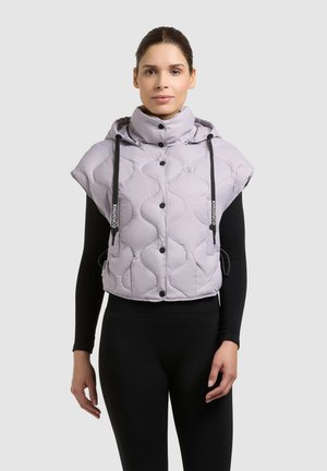 Kvinde iført en lysegrå quiltet dunvest uden ærmer med høj krave og sorte snore over en tætsiddende sort langærmet top.