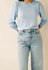 Pull bleu clair à col rond avec des manches bouffantes, associé à un jean en denim clair taille haute. Texture tricot douce, coupe décontractée.