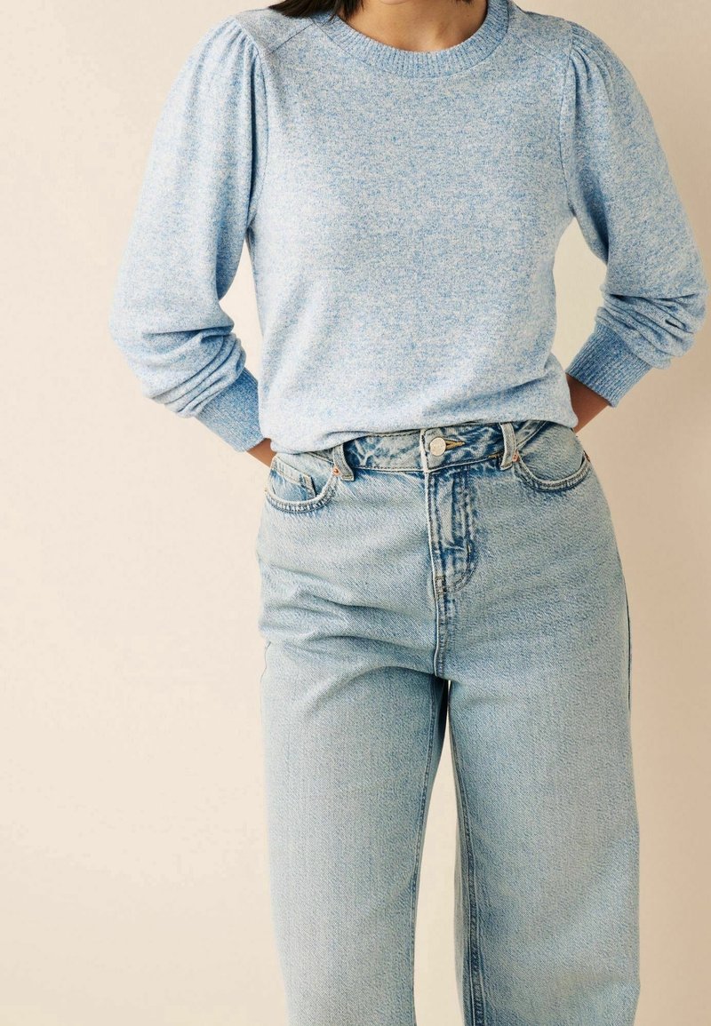 Pull bleu clair à col rond avec des manches bouffantes, associé à un jean en denim clair taille haute. Texture tricot douce, coupe décontractée.
