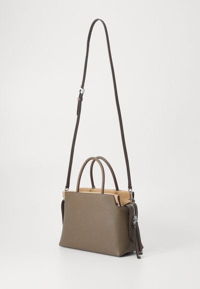 Sac à main en cuir marron avec deux poignées supérieures, une bandoulière amovible et un intérieur beige. Il dispose d'une fermeture éclair et d'un détail en frange sur le côté.