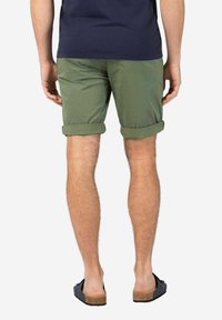 Green cotton shorts with rolled cuffs, featuring a back view, paired with dark sandals. The fabric appears smooth with a matte finish.