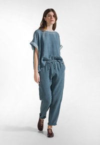 Loszittende, zachte blauwe linnen outfit met korte mouwen en een taille met trekkoord; gecombineerd met bruine veterschoenen; minimalistisch ontwerp.