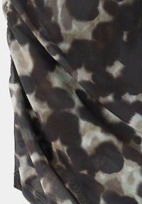 Gros plan d’un tissu à motif camouflage sombre avec une texture fine en maille et des coutures visibles sur les bords pliés.