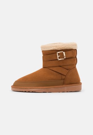 Brauner Wildleder-Stiefelette mit weichem Fellfutter, verstellbarem Schnallenriemen und Gummisohle, entworfen für Komfort und Wärme.