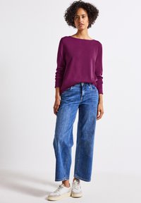 Lila Langarmoberteil, lockere Passform, kombiniert mit hellblauenweit geschnittenen Jeans und weißen Sneakers, die ein lässiges Outfit kreieren.