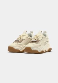 Beige sportiga sneakers med mesh och släta material, rundade tår och texturerad sula. Har snören och en dragflik vid hälen.