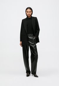 Blazer oversized preto, suéter canelado preto, calças de pele falsa pretas de cintura alta e sapatos de salto agudo, todos num estilo elegante e monocromático.