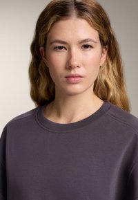 Felpa grigia con collo a giro e accenti a coste, caratterizzata da una texture morbida e una vestibilità rilassata, che mette in evidenza linee pulite e un design minimal.