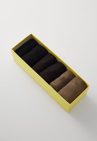Set of six rolled socks in a yellow box, featuring a gradient of dark to light brown shades with a smooth texture and discreet logo.