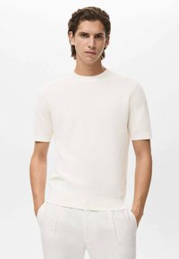 Witte gebreide crewneck t-shirt met korte mouwen, geribbelde textuur en een relaxte pasvorm, gecombineerd met lichtgekleurde broek.