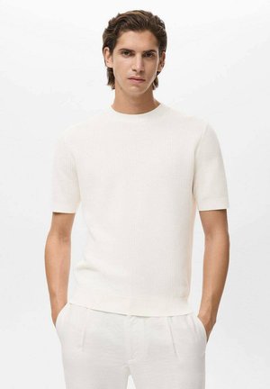 White knit crewneck t-shirt with short sleeves, ribbed texture, and a relaxed fit, paired with light-colored pants.