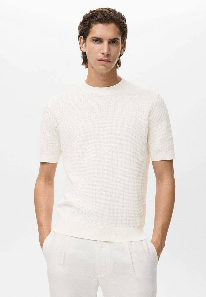 Witte gebreide crewneck t-shirt met korte mouwen, geribbelde textuur en een relaxte pasvorm, gecombineerd met lichtgekleurde broek.