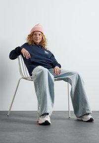 La felpa navy presenta un logo, abbinata a jeans oversize azzurri chiari. Un berretto di lana rosa completa le sneakers bianche con dettagli neri.