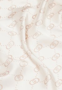 Tela de seda con un fondo color crema claro, adornada con un patrón sutil en beige que presenta formas ovales entrelazadas y líneas punteadas en repetición.