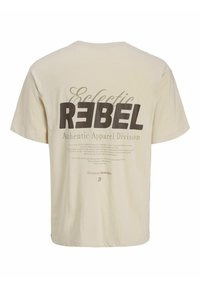 T-shirt beige avec un grand texte audacieux "REBEL" et un texte plus petit "Eclectic Authentic Apparel Division" ainsi qu'un texte imprimé supplémentaire au dos.