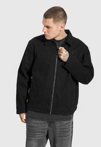 Czarna kurtka na zamek wykonana z mocnego materiału. Posiada spiczasty kołnierz, boczne kieszenie i subtelne haftowane logo na piersi.