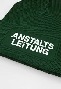 Green knit beanie with ribbed texture, featuring a white rectangular patch that reads "ANSTALTSLEITUNG" in bold font.