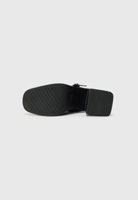 Black shoe sole with a square heel. Features a textured grip pattern and a smooth, rounded front. Simple design, minimal additional details.